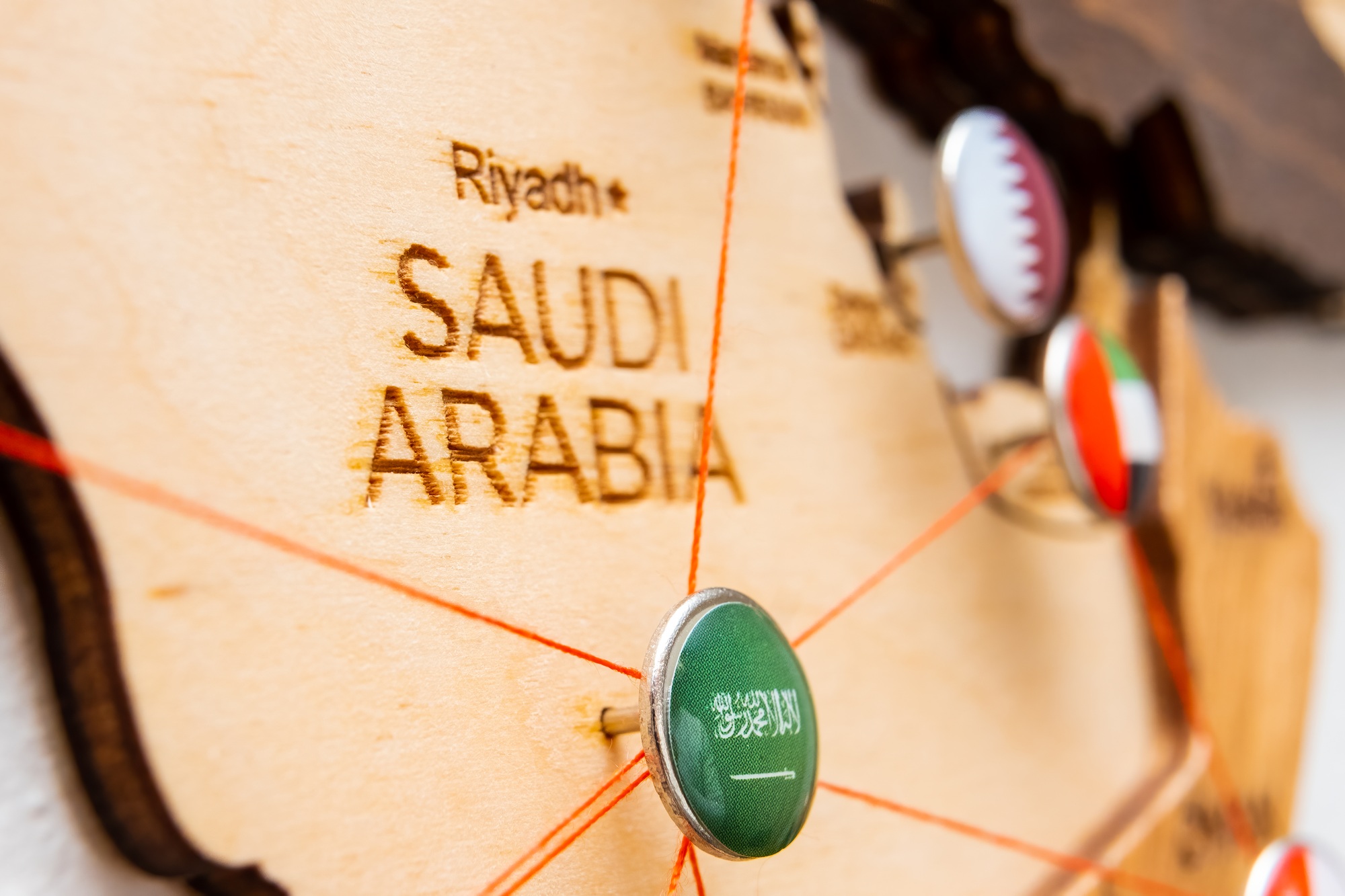 Saudi Arabia flag on the pushpin and red threads on the wooden map